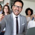 uomo con un computer in mano che esulta e dietro di lui persone che sorridono
