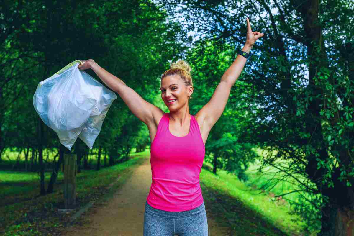 Donna in tenuta sportiva all'interno di un parco che tiene in mano un sacchetto di spazzatura