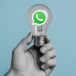 Illustrazione di una mano che tiene una lampadina (idea) e logo WhatsApp all'interno